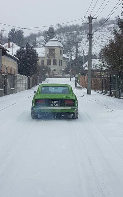 Green 1971 Datsun 240Z from behind on a snow-covered village street, driven through winter
