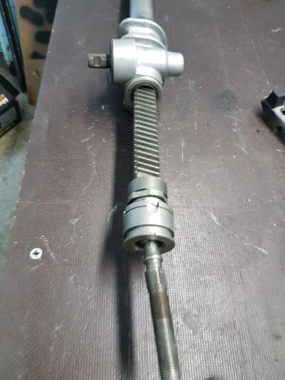Rebuilt Datsun 240Z steering rack on a workbench, showing the pinion housing, rack teeth and coupling