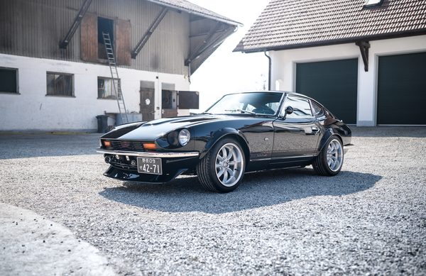 Front three-quarter of a black 1975 Datsun 280Z widebody with chrome bumper and flared front arches