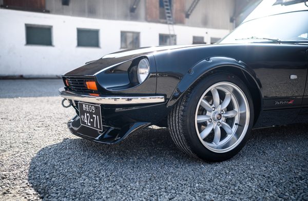 Flared front arch of a black 1975 Datsun 280Z sitting over a 17-inch multi-spoke wheel