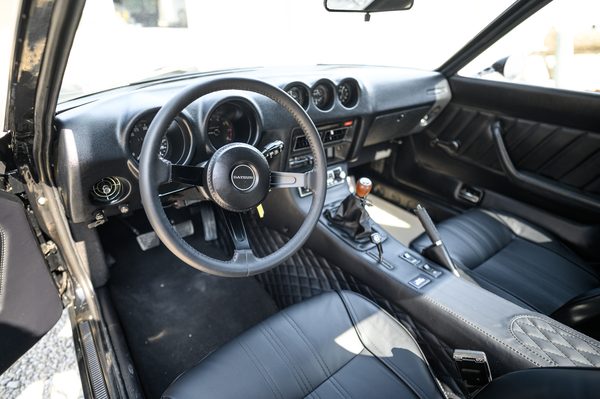 Interior of a 1975 Datsun 280Z showing the dashboard, centre gauges and wood-rimmed steering wheel