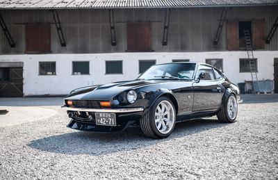 Black Datsun 280Z widebody front three-quarter in front of a farm building