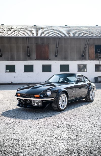 Black Datsun 280Z widebody front three-quarter beside a farm building