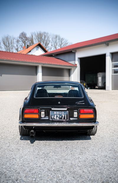 Rear end of a black Datsun 280Z with tail lights and chrome bumper