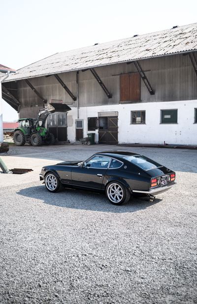 Black Datsun 280Z widebody from the rear three-quarter on a gravel yard