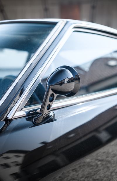 Chrome bullet wing mirror on the door of a black Datsun 280Z
