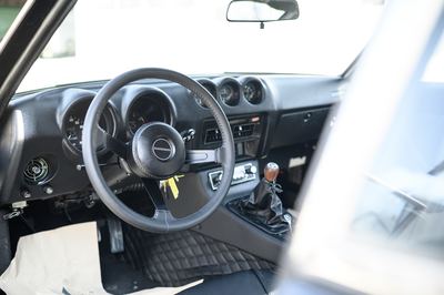 Dashboard and steering wheel of a Datsun 280Z seen through the open door