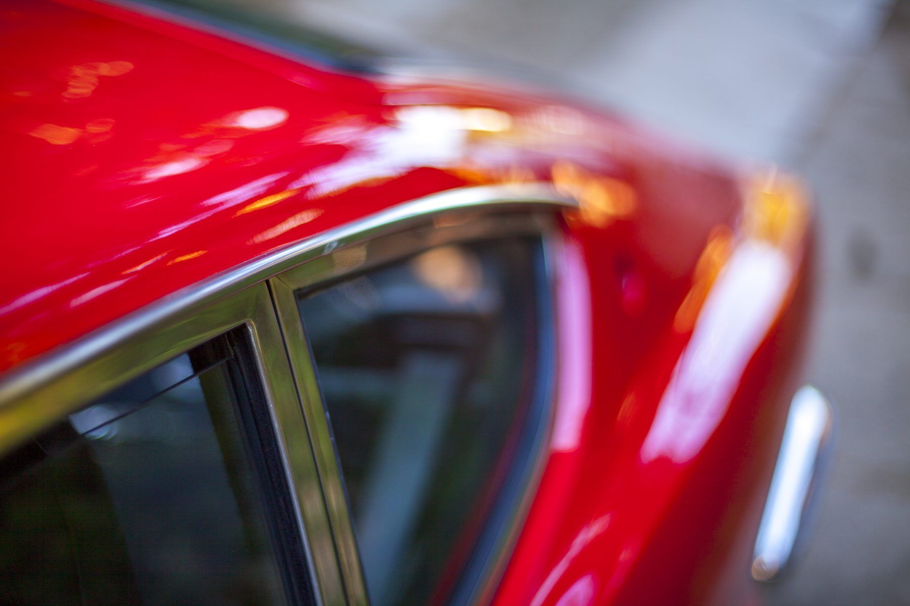 Close-up of a red 1976 Datsun 280Z roofline, chrome window trim catching the light along the door frame