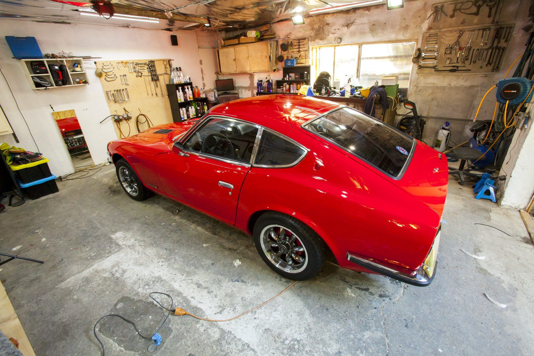 Red 1976 Datsun 280Z photographed side-on in a workshop, showing the full S30 profile from front wing to rear hatch