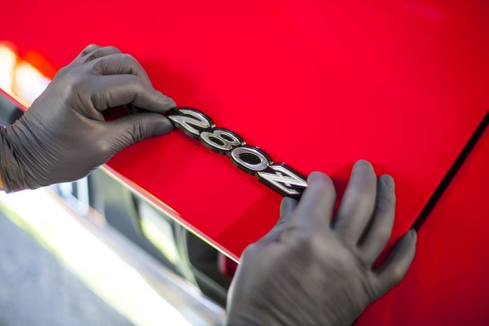 Gloved hands fitting a 280Z badge to red bodywork during final assembly