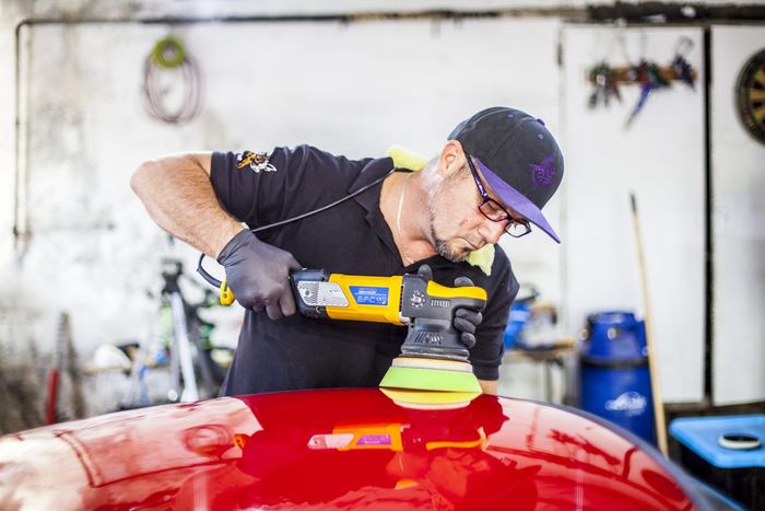 Machine polishing the bonnet of a red Datsun 280Z during paint correction