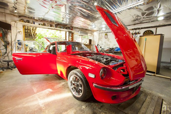 Red Datsun 280Z with the bonnet raised, front quarter view in the workshop
