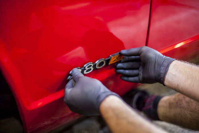 Badge being offered up to the rear quarter panel of a red Datsun 280Z