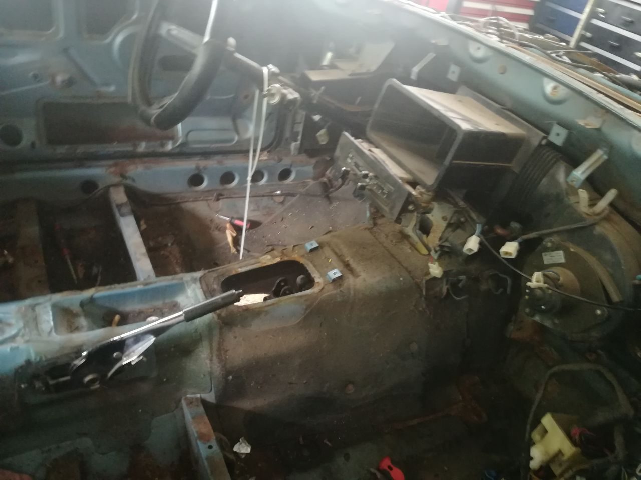 Datsun 280Z floorpan with wiring loom laid out during strip-down, surface rust visible on the bare metal