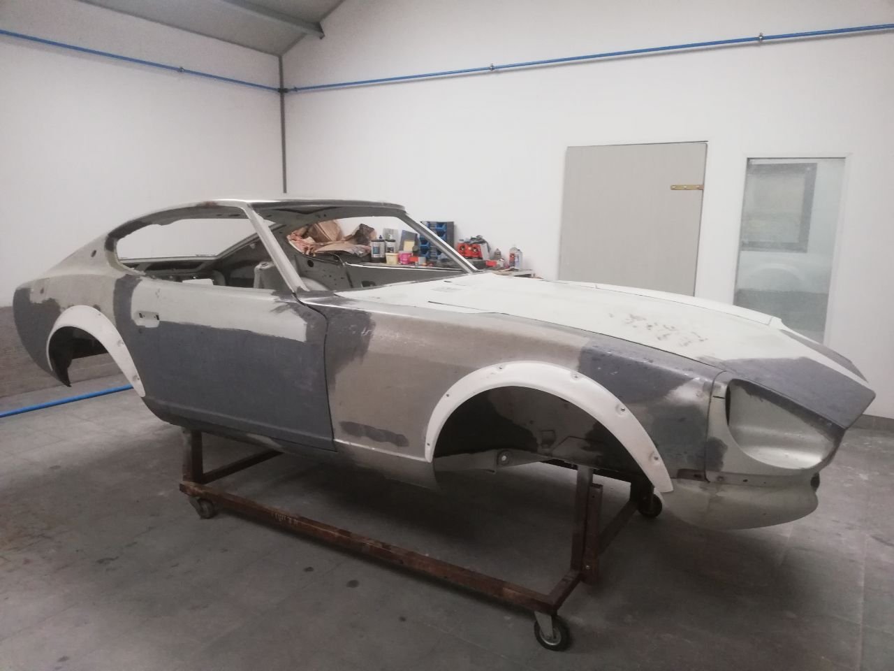 1976 Datsun 280Z widebody shell in primer on a rolling frame in the paint booth, flared arches fitted, ready for paint
