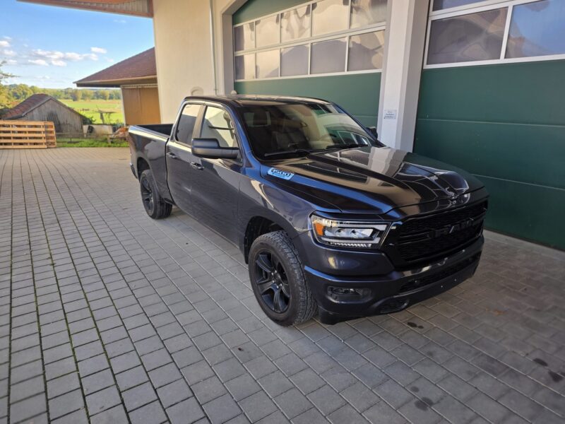 ram-1500-big-horn-2021-4x4-quad-cab-vorne-rechts-02 RAM 1500 Big Horn 2021 Quad Cab 4x4 in Maximum Steel Metallic vor grünem Hallentor, Frontansicht schräg rechts